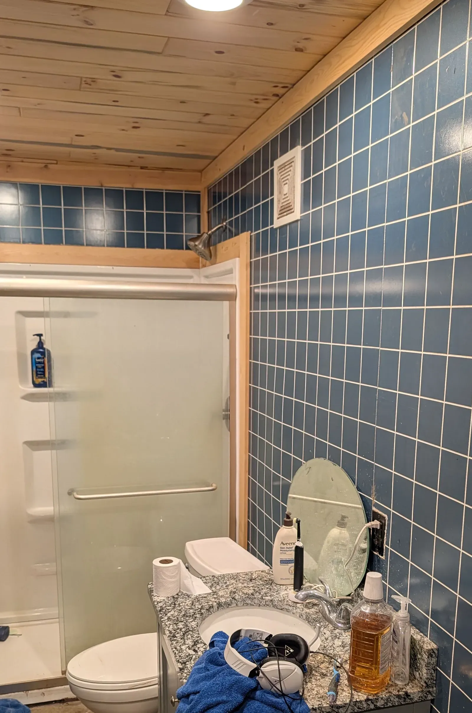 Original bathroom with blue tile walls, pine ceiling, and dated shower stall